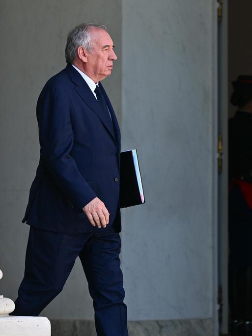 François Bayrou verlässt, eine Aktenmappe unter seinem Arm, ein Regierungsgebäude.