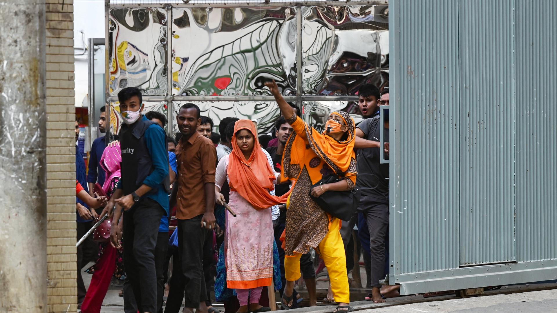Arbeiter und Arbeiterinnen einer Textilfabrik in Bangladesch stehen an einem Fabriktor und fordern mehr Geld.