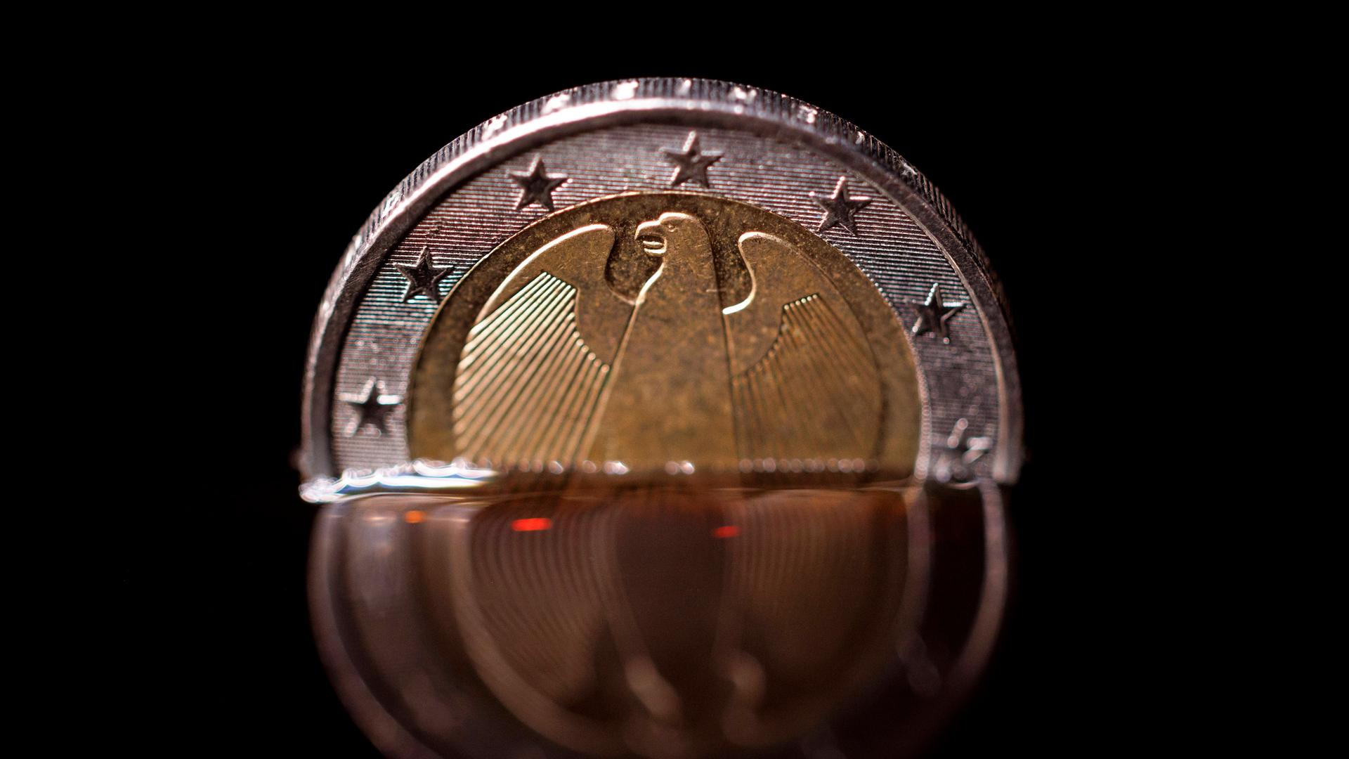 Eine 2-Euro-Münze taucht in eine schwarze Flüssigkeit ein. 