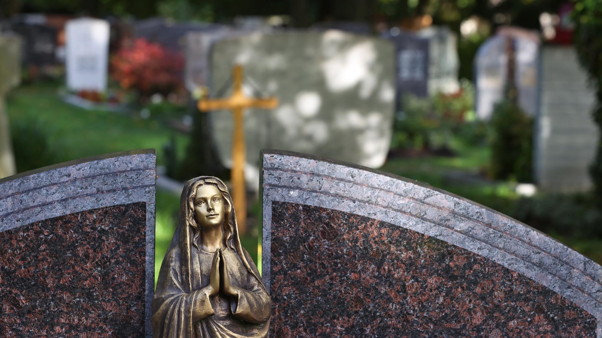 Eine Engelsfigur steht auf einem Friedhof vor Grabsteinen. 