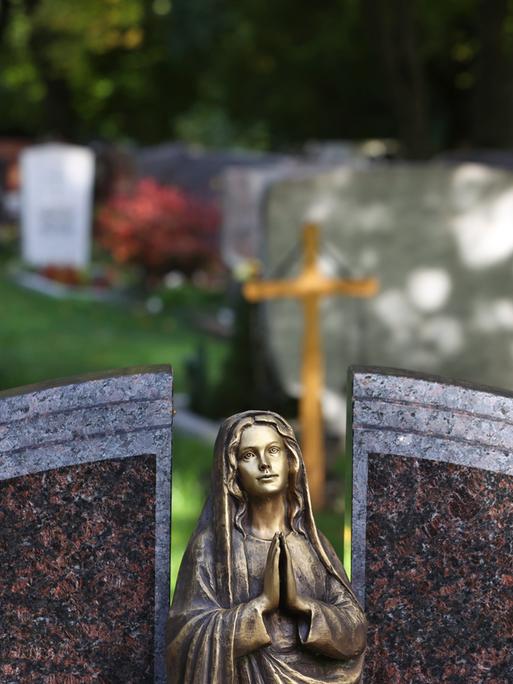 Eine Engelsfigur steht auf einem Friedhof vor Grabsteinen. 