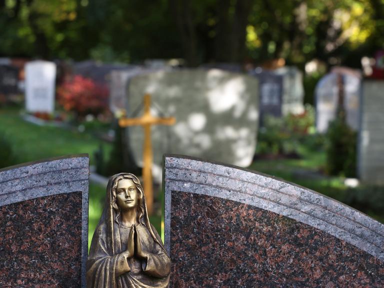 Eine Engelsfigur steht auf einem Friedhof vor Grabsteinen. 