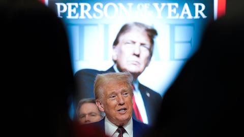 Donald Trump steht vor einem überdimensional großen hinterleuchteten Cover des Time-Magazin auf dem er selbst zu sehen ist, darüber steht "Person of the Year".