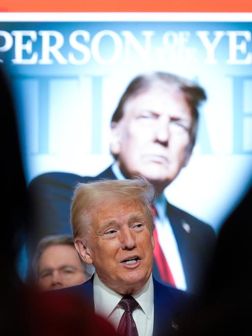 Donald Trump steht vor einem überdimensional großen hinterleuchteten Cover des Time-Magazin auf dem er selbst zu sehen ist, darüber steht "Person of the Year".