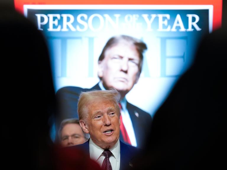 Donald Trump steht vor einem überdimensional großen hinterleuchteten Cover des Time-Magazin auf dem er selbst zu sehen ist, darüber steht "Person of the Year".