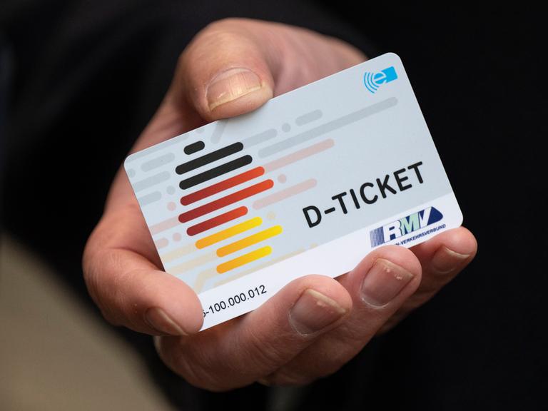 Eine Hand hält eine Plastik-Karte in die Kamera. Darauf steht "D-Ticket". Und man sieht eine Karte von Deutschland. Die Karte hat die Farben schwarz-rot-gelb.