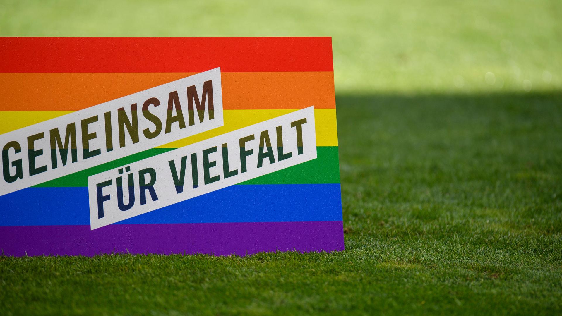 Ein Aufsteller in Regenbogenfarben mit der Aufschrift "Gemeinsam für Vielfalt" steht auf dem Rasen in einem Fußballstadion.