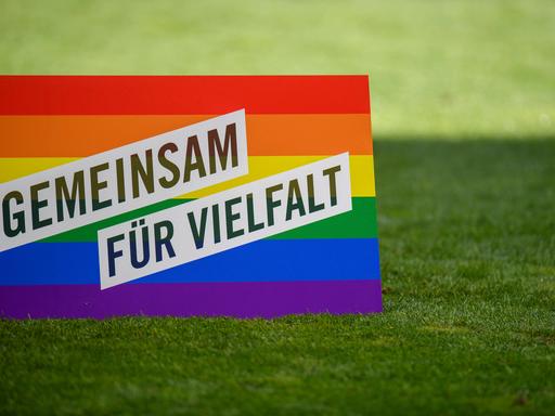 Ein Aufsteller in Regenbogenfarben mit der Aufschrift "Gemeinsam für Vielfalt" steht auf dem Rasen in einem Fußballstadion.