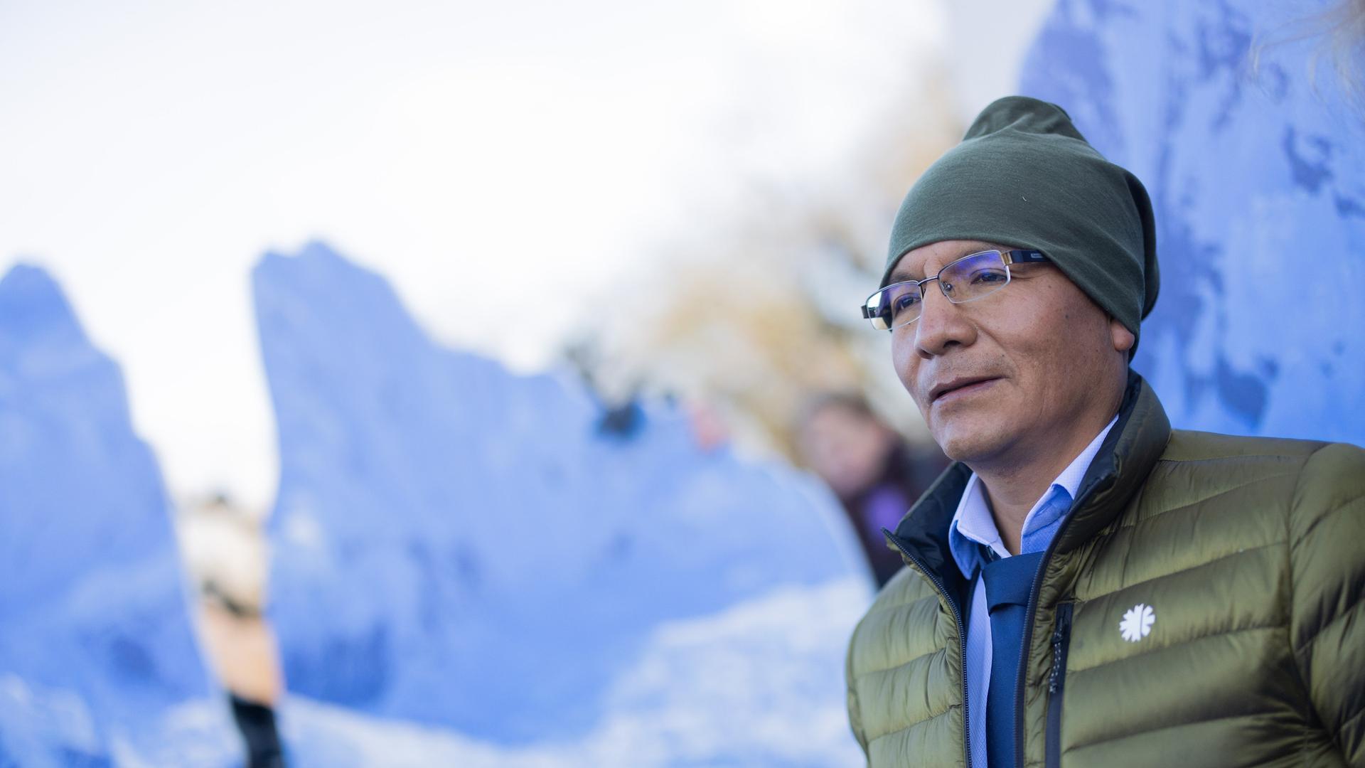 Der peruanische Bergbauer und Bergführer Saul Luciano Lliuya vor einem Foto einer winterlichen Berglandschaft Der peruanische Bergbauer und Bergführer Saul Luciano Lliuya vor einem Foto einer winterlichen Berglandschaft