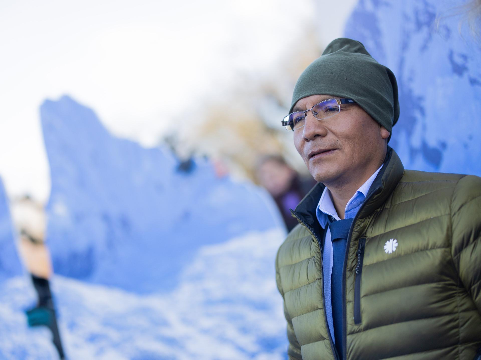 Der peruanische Bergbauer und Bergführer Saul Luciano Lliuya vor einem Foto einer winterlichen Berglandschaft 