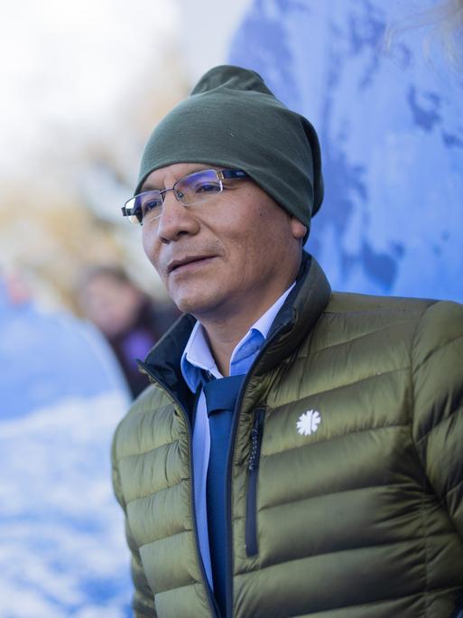 Der peruanische Bergbauer und Bergführer Saul Luciano Lliuya vor einem Foto einer winterlichen Berglandschaft 