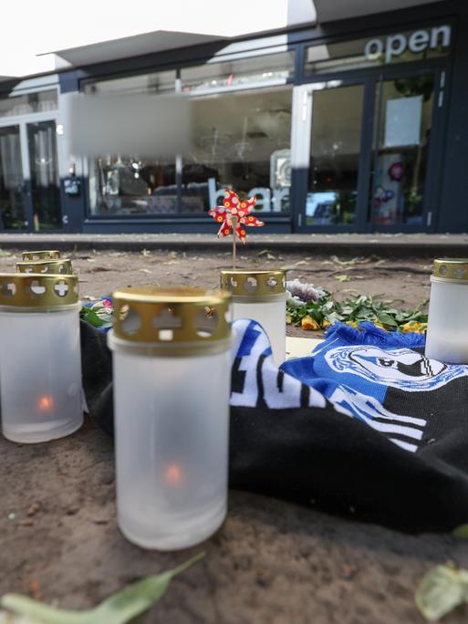Kerzen und ein Fanschal von Arminia Bielefeld sind an einem Tatort in der Innenstadt zu sehen. Nach dem Angriff eines Mannes auf mindestens fünf Menschen vor einer Bar in Bielefeld ist ein Tatverdächtiger festgenommen worden.