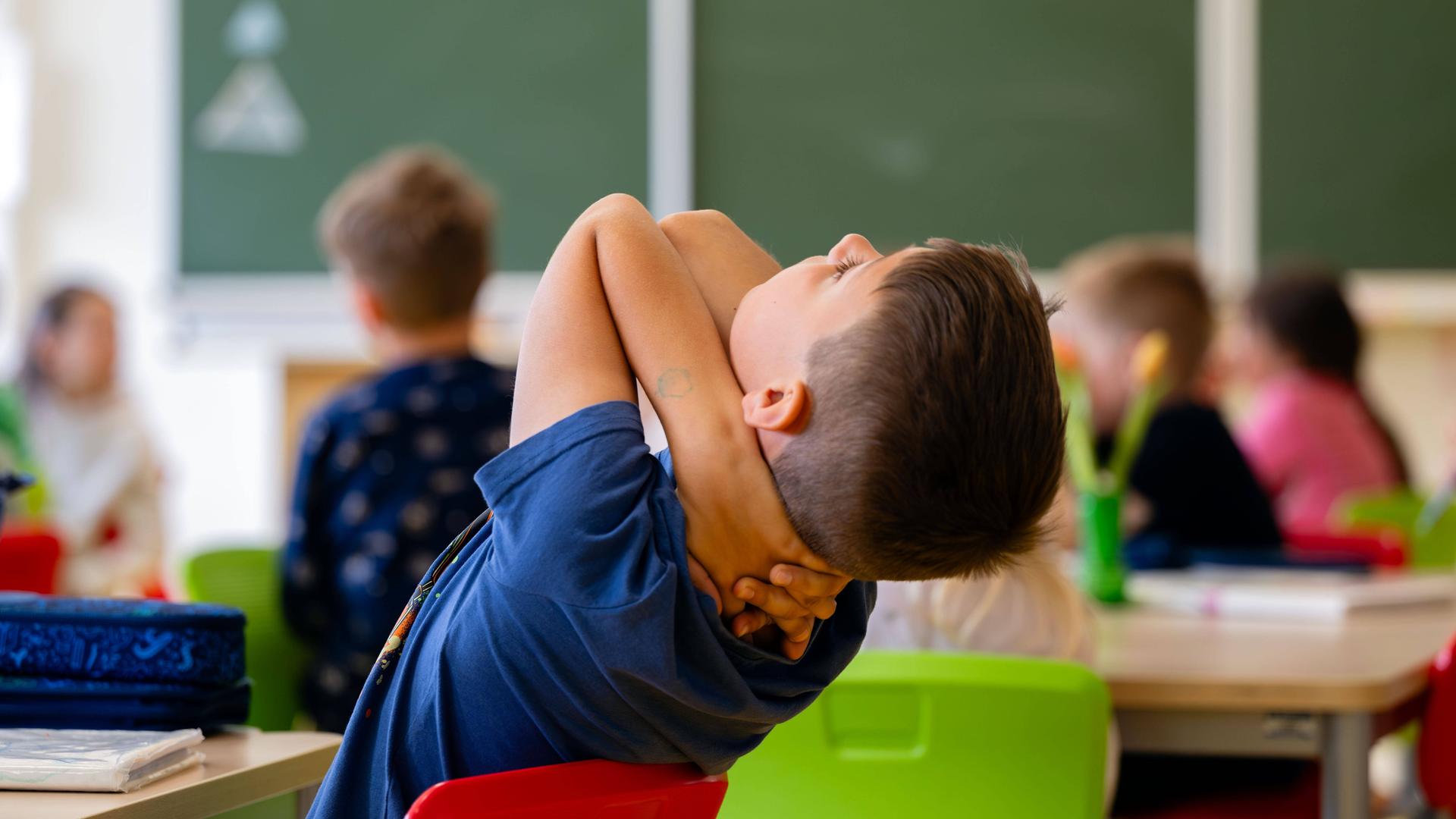Ein Junge lehnt sich in einem Klassenzimmer auf seinem Stuhl zurück und schraut in Richtung Decke. Ein Junge lehnt sich in einem Klassenzimmer auf seinem Stuhl zurück und schraut in Richtung Decke.