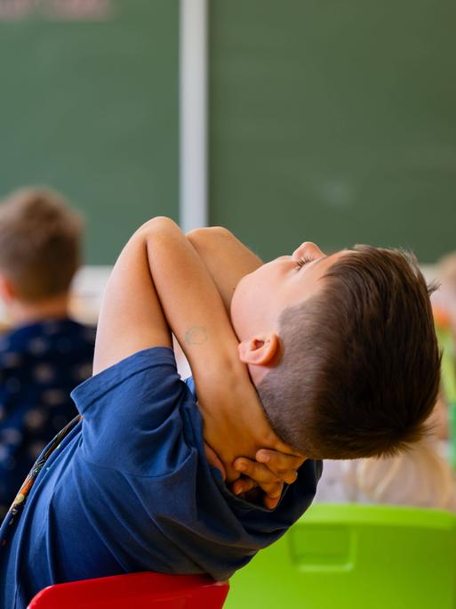 Ein Junge lehnt sich in einem Klassenzimmer auf seinem Stuhl zurück und schraut in Richtung Decke.