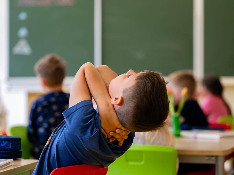 Ein Junge lehnt sich in einem Klassenzimmer auf seinem Stuhl zurück und schraut in Richtung Decke. Ein Junge lehnt sich in einem Klassenzimmer auf seinem Stuhl zurück und schraut in Richtung Decke.