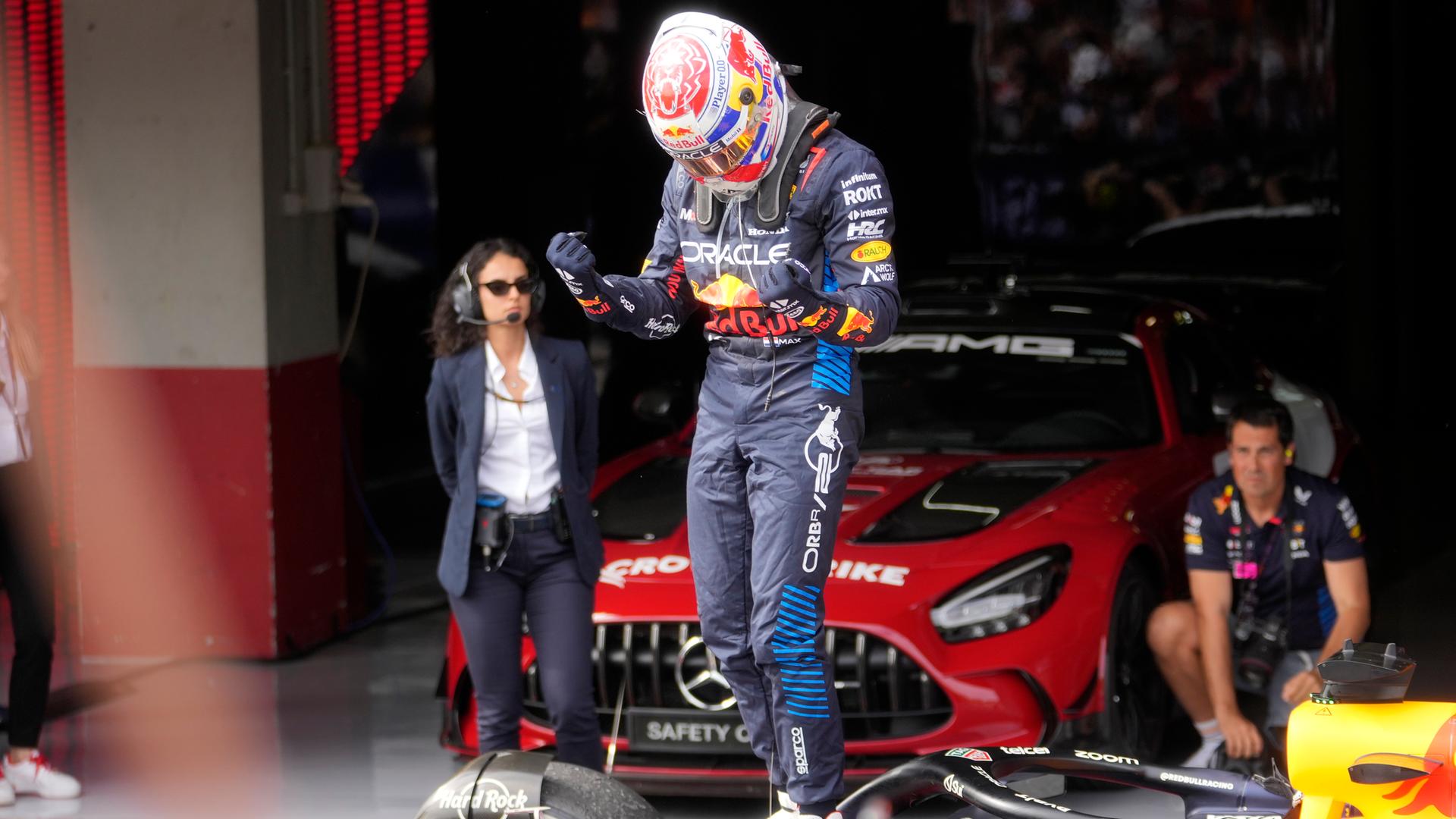 Verstappen mit Helm und Rennfahrer-Dress steht auf seinem Rennwagen und ballt die Fäuste. Dahinter ein Mann und eine Frau. 