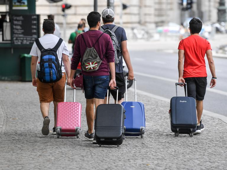 Touristen gehen mit Rollkoffern einen Gehweg in Berlin-Mitte entlang.