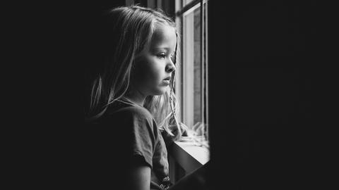 Ein Mädchen schaut traurig aus dem Fenster. 