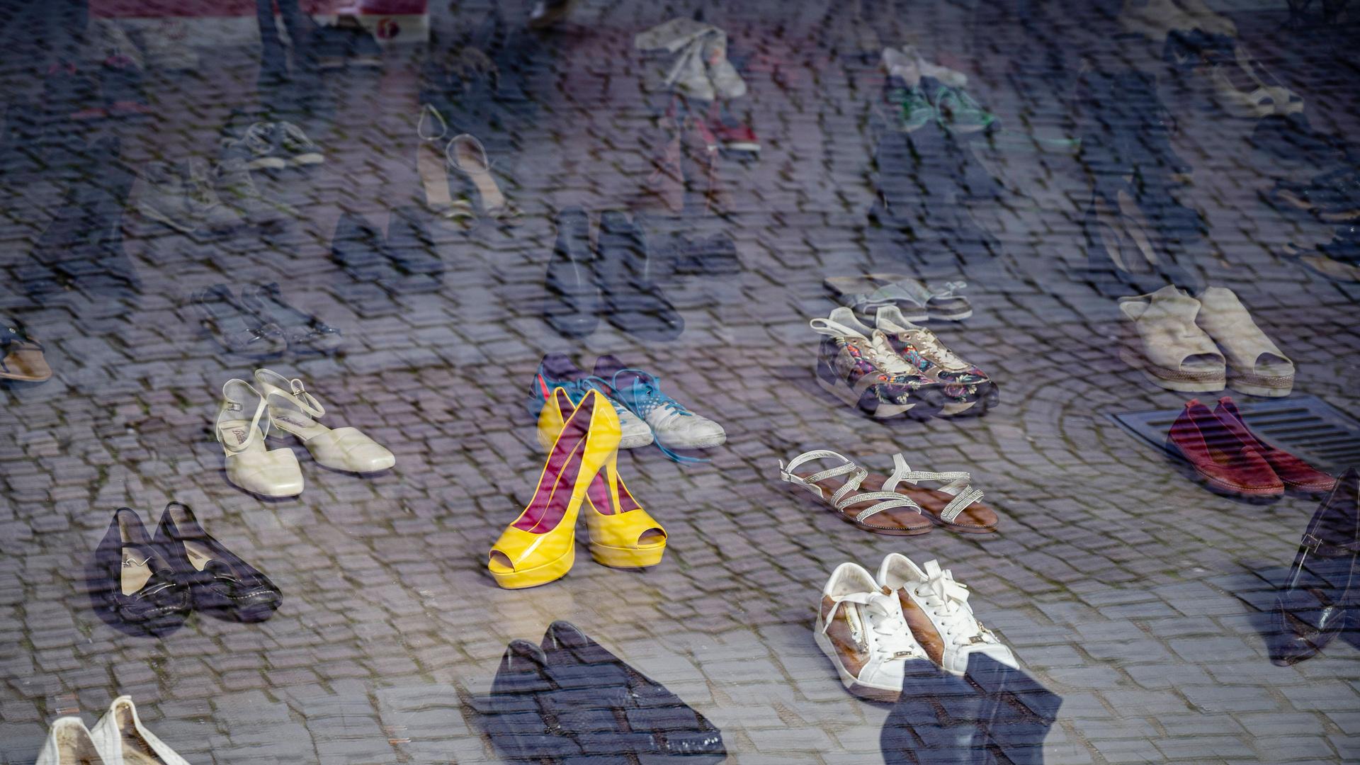 Hinter einer Fensterscheibe stehen eine ganze Menge von Schuhpaaren. Sie sind in Richtung des Betrachters ausgerichtet.