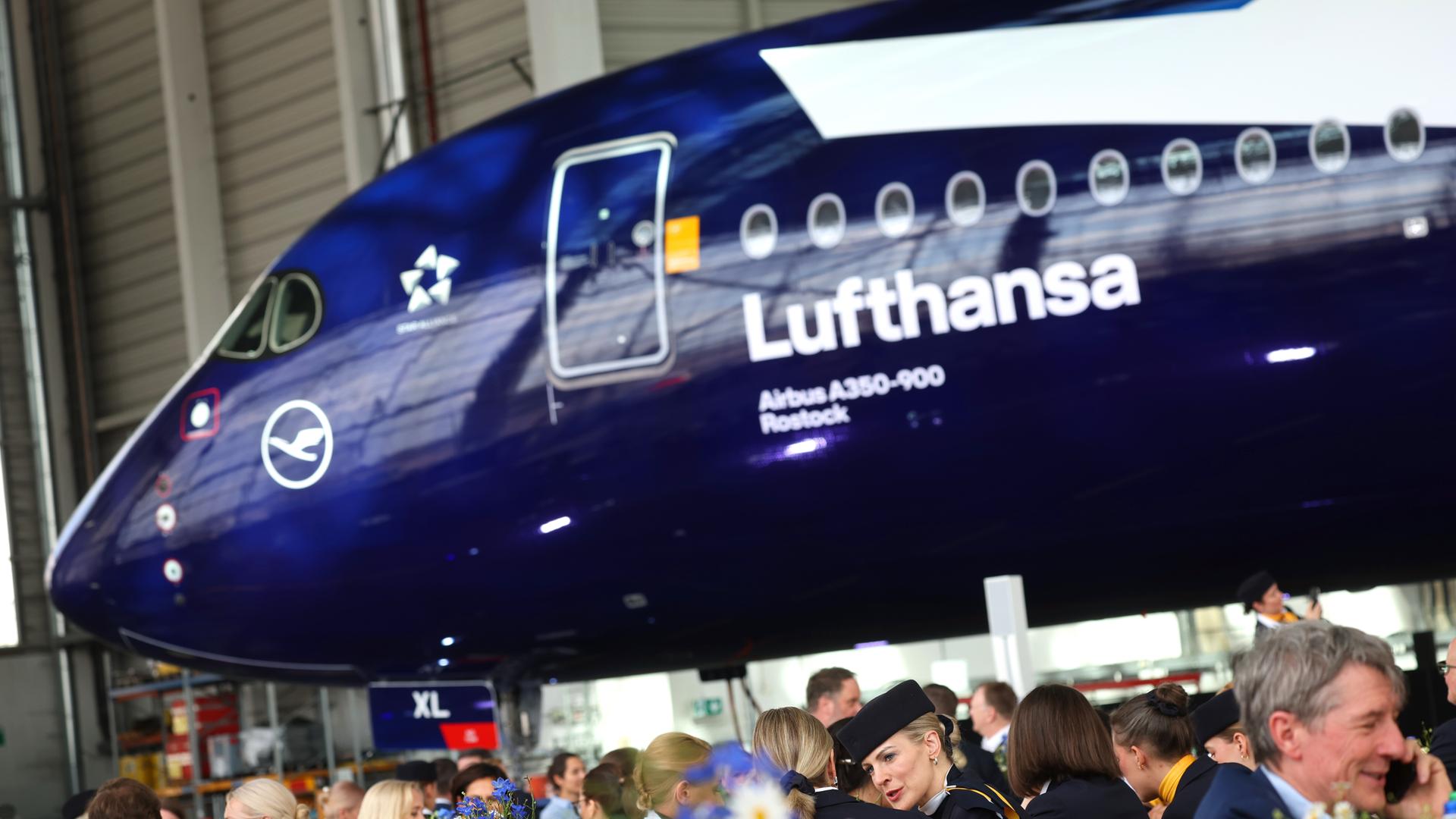 Mitarbeiter und Gäste sitzen bei der Feier zum 100-jährigen Bestehen der Lufthansa, vor dem Airbus A350-900 Rostock.