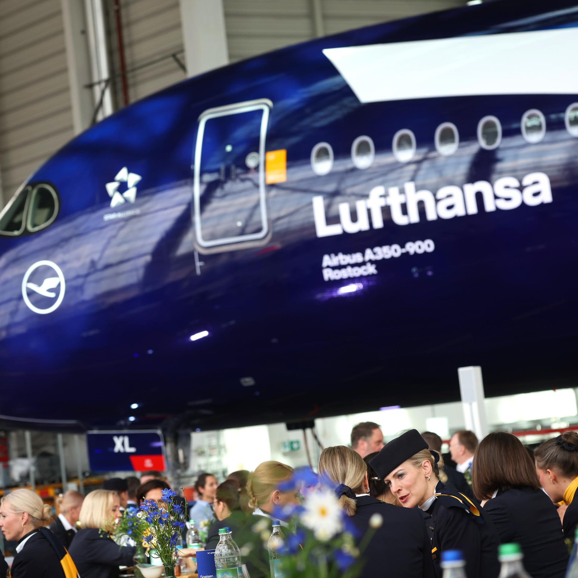 Mitarbeiter und Gäste sitzen bei der Feier zum 100-jährigen Bestehen der Lufthansa, vor dem Airbus A350-900 Rostock.