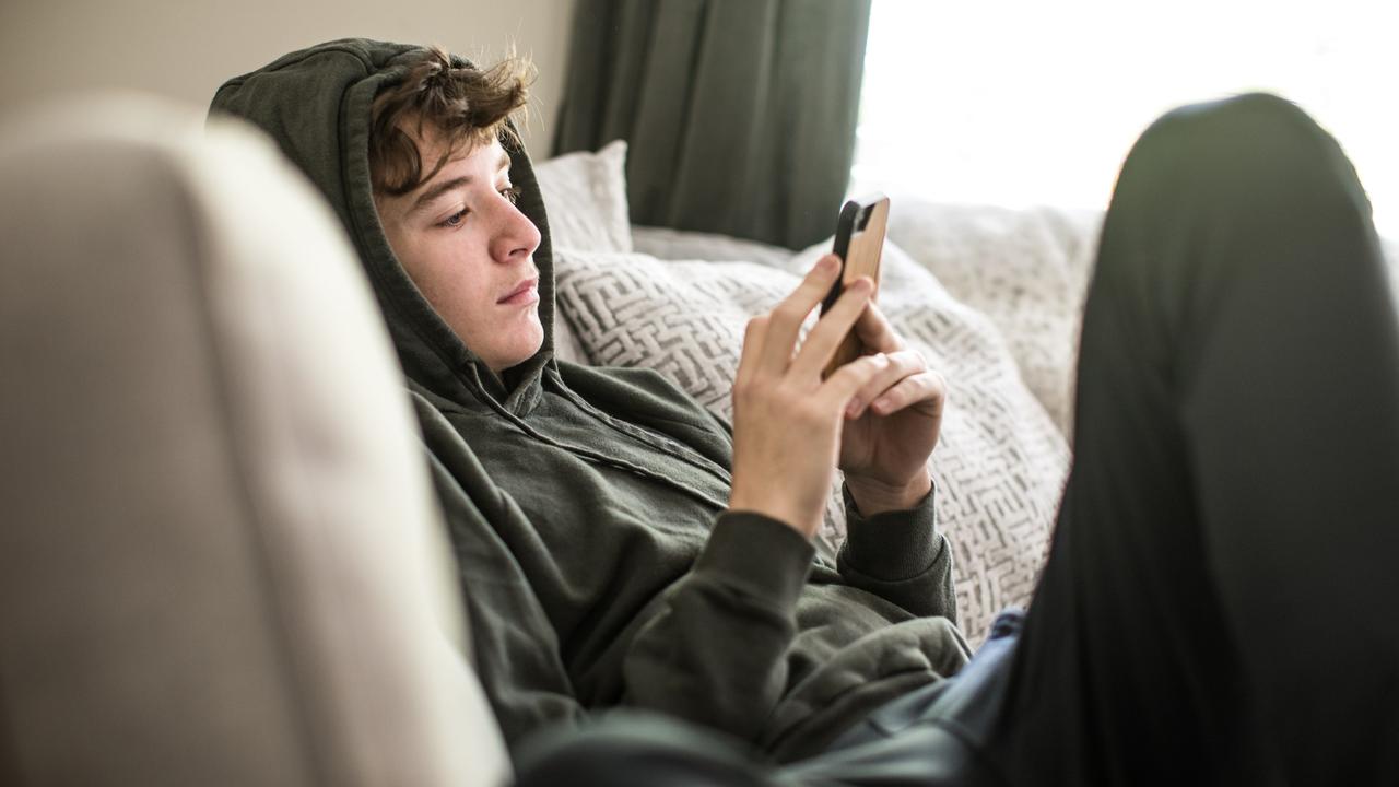 Ein Teenager sitzt auf der Couch und schaut auf sein Smartphone.