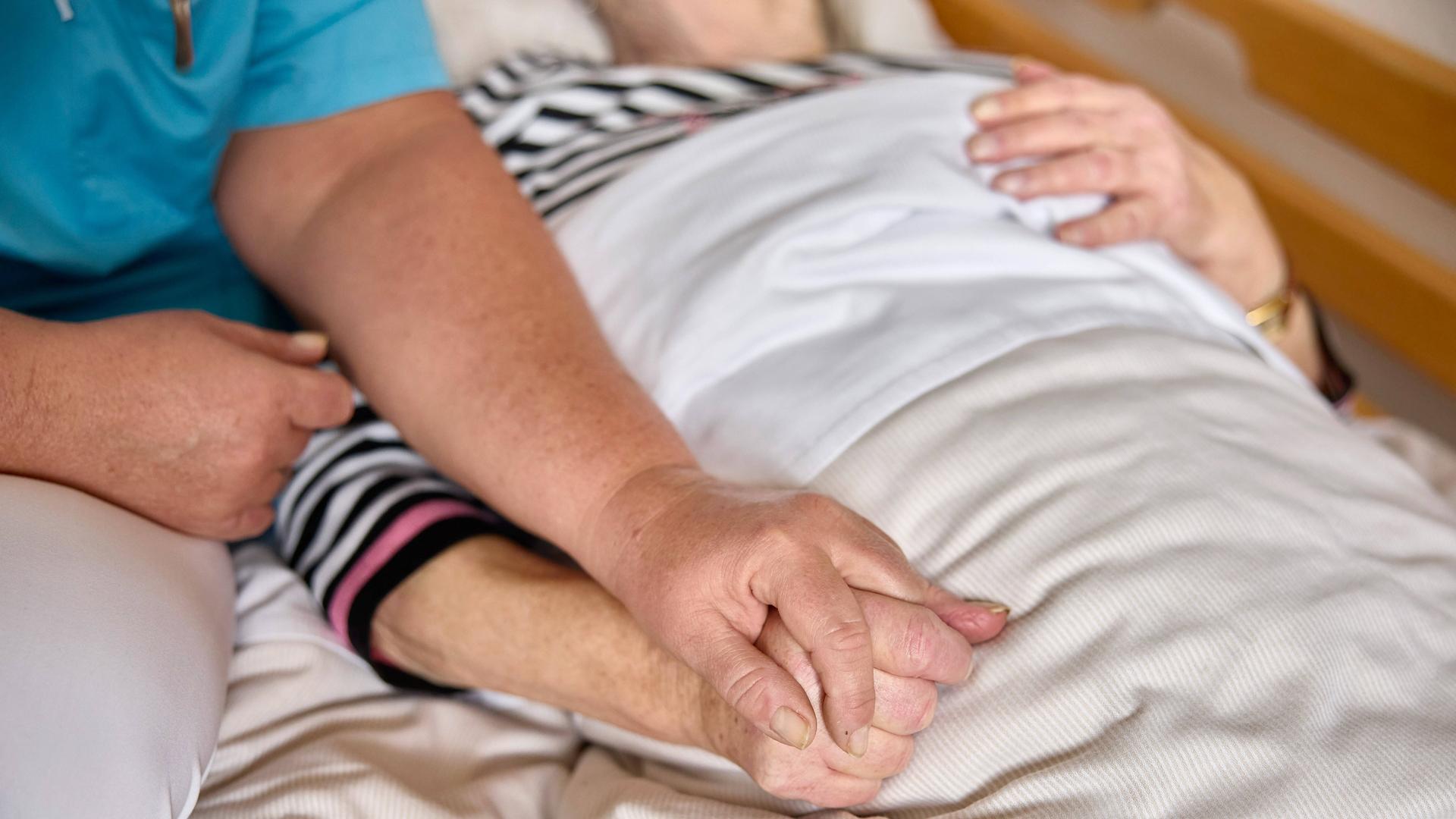 Pflegekraft mit einer Bewohnerin auf der Palliativstation in einem Pflegeheim. Die Pflegerin hält die Hand der alten Frau.