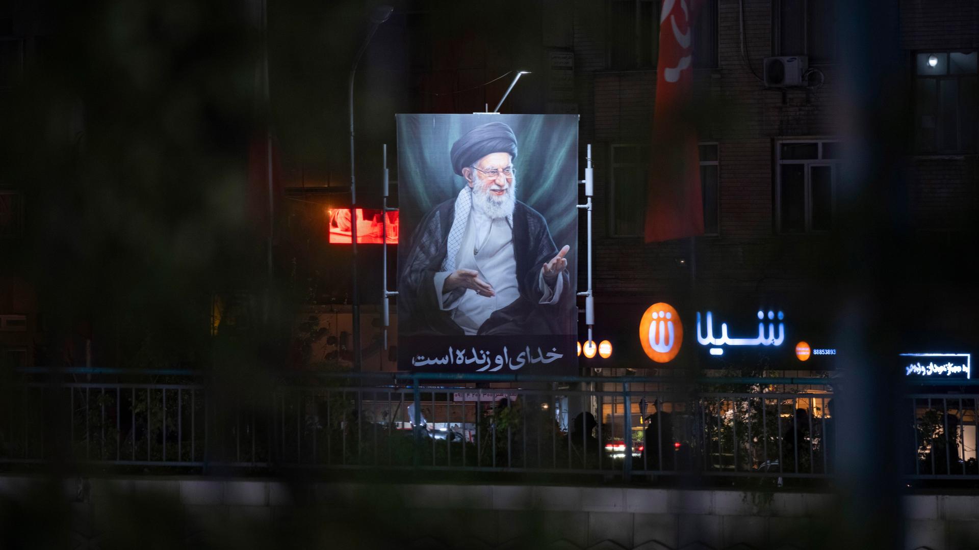 Ein beleuchtetes Porträt des am ersten Kriegstages getöteten geistlichen Führers, Ajatollah Ali Chamenei in den ansonsten größtenteils dunklen Straßen Teherans