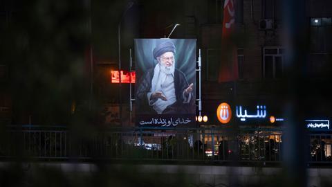 Ein beleuchtetes Porträt des am ersten Kriegstages getöteten geistlichen Führers, Ajatollah Ali Chamenei in den ansonsten größtenteils dunklen Straßen Teherans