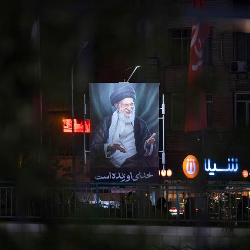 Ein beleuchtetes Porträt des am ersten Kriegstages getöteten geistlichen Führers, Ajatollah Ali Chamenei in den ansonsten größtenteils dunklen Straßen Teherans