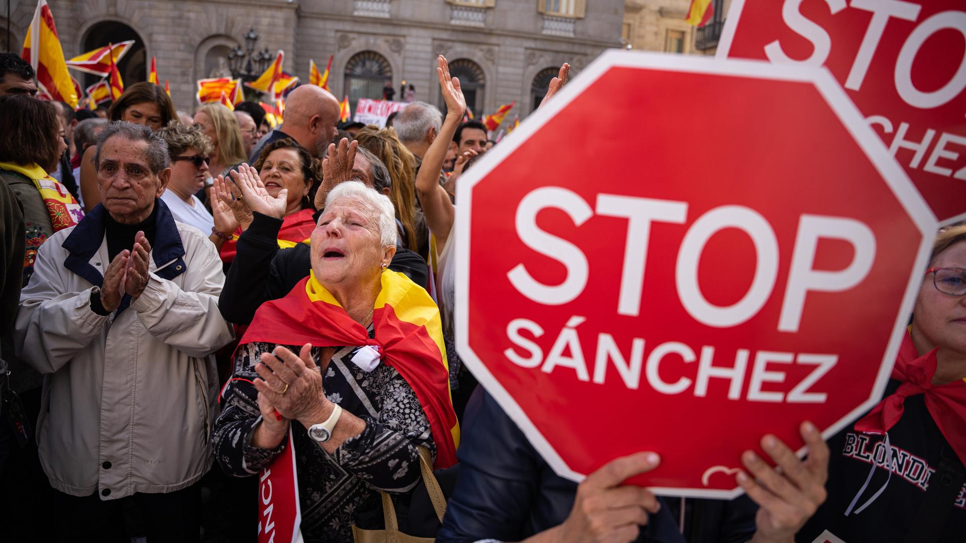 Demonstranten halten rote Pappschilder hoch, auf denen "Stop Sánchez" steht: Tausende protestieren in Barcelona gegen das Amnestiegesetz für katalanische Separatisten.

