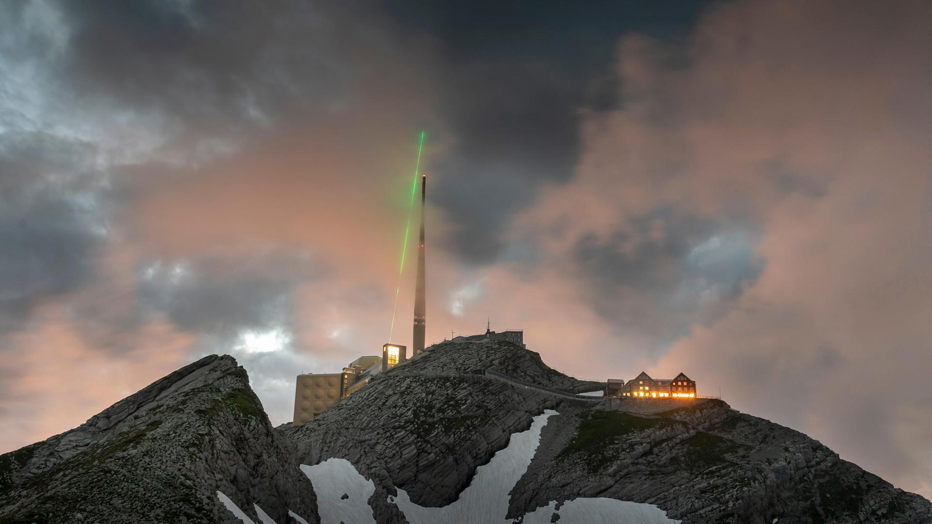 Ein grüner Laser strahlt von der Bergspitze des Säntis in den Himmel.