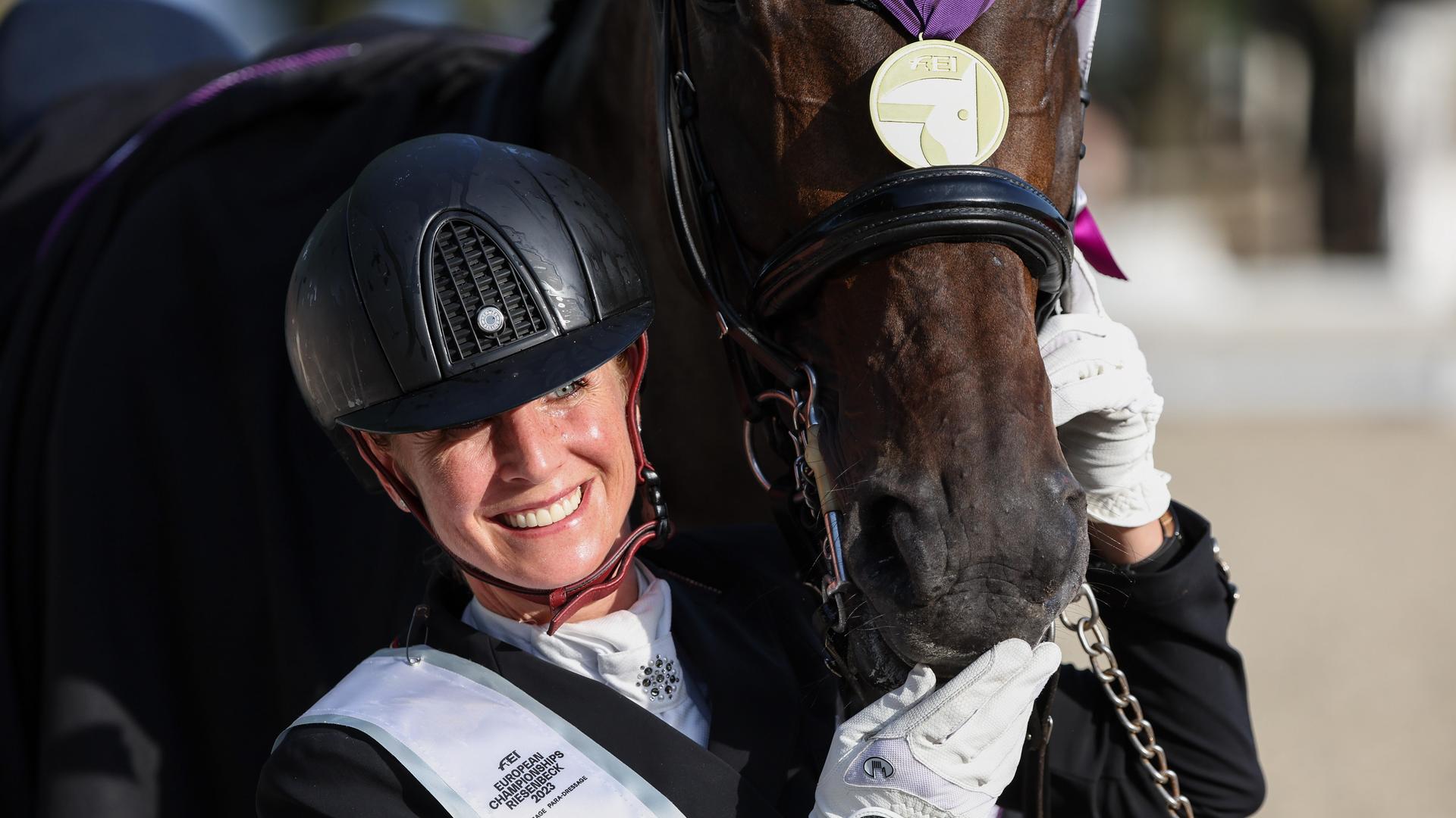 Dressurreiterin Jessica von Bredow-Werndl streichelt ihr Pferd, das eine Goldmedaille auf dem Nasenrücken umgehängt hat. Dressurreiterin Jessica von Bredow-Werndl streichelt ihr Pferd, das eine Goldmedaille auf dem Nasenrücken umgehängt hat.