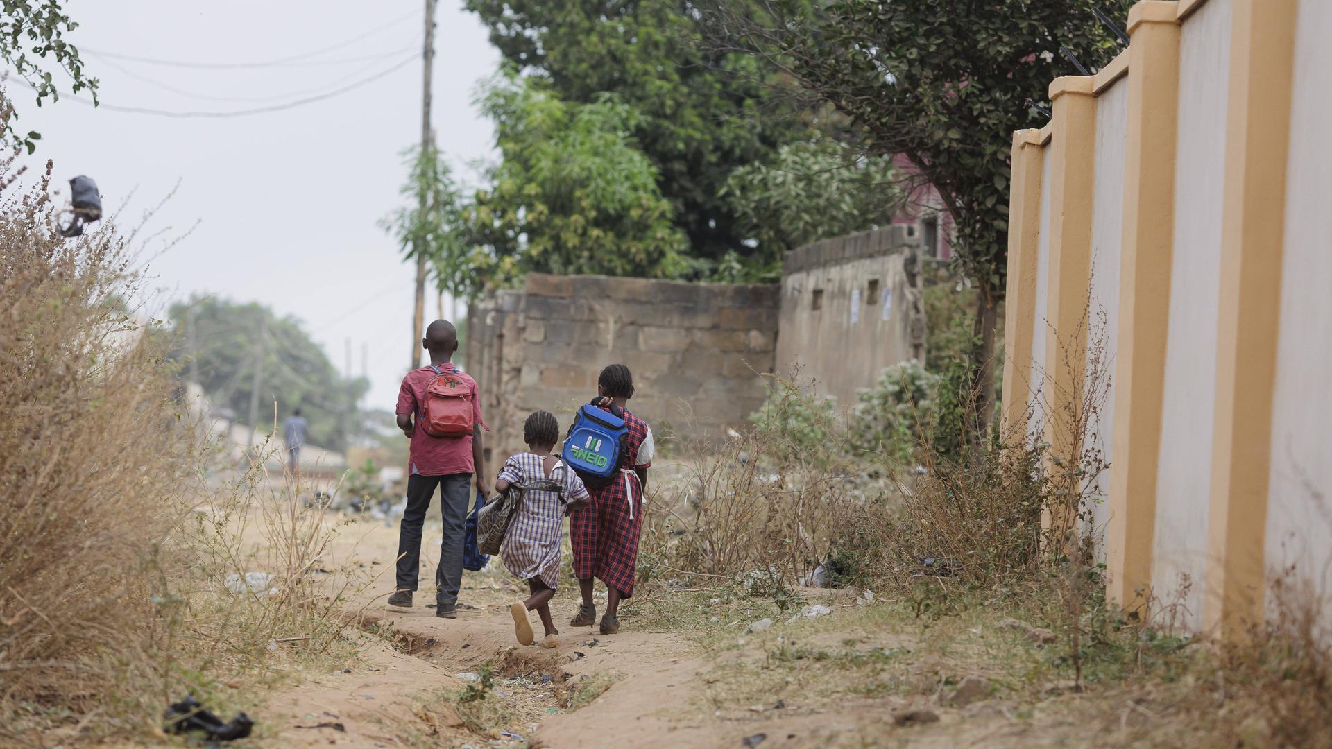Drei Schulkinder gehen auf einem Weg aus Sand.
