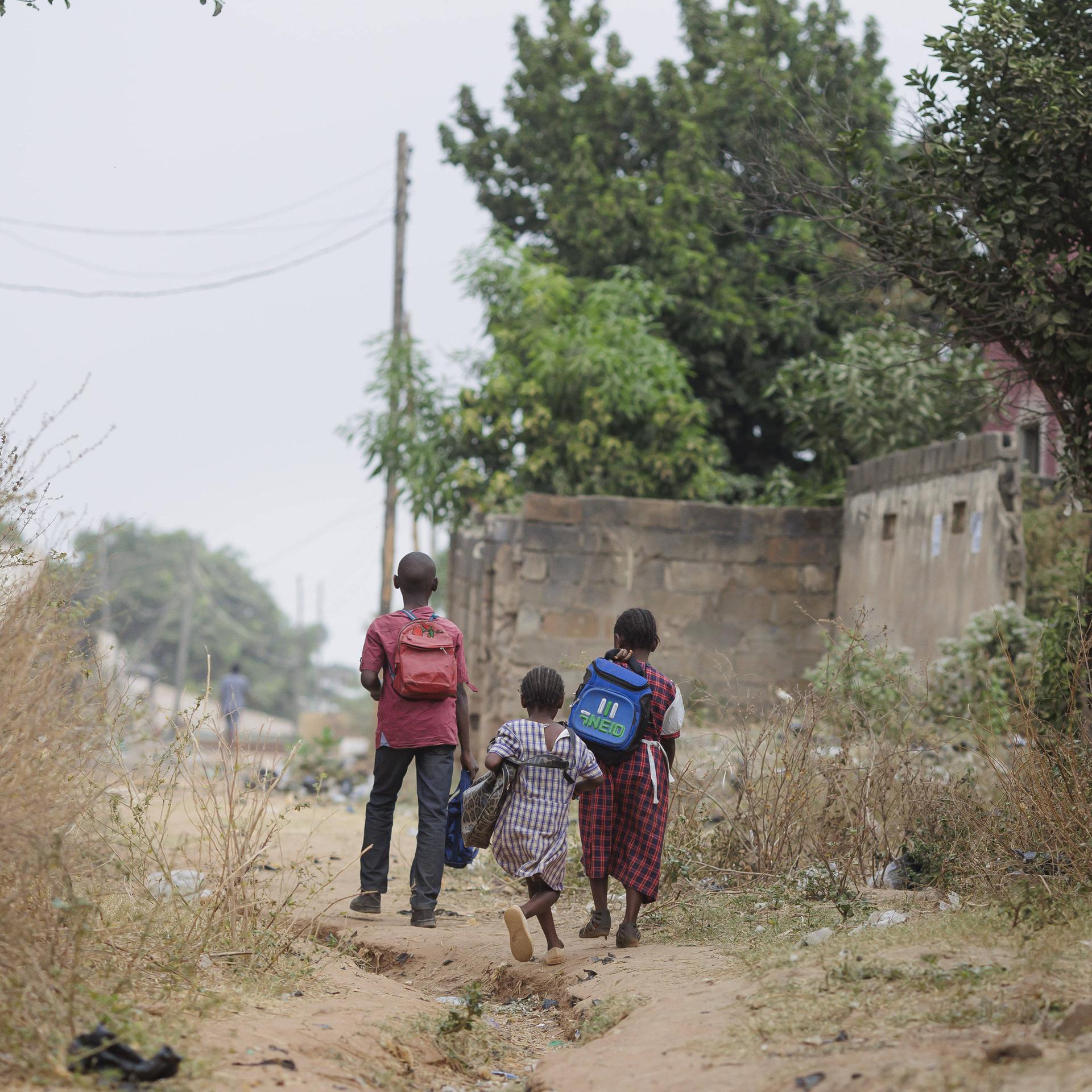 Drei Schulkinder gehen auf einem Weg aus Sand.