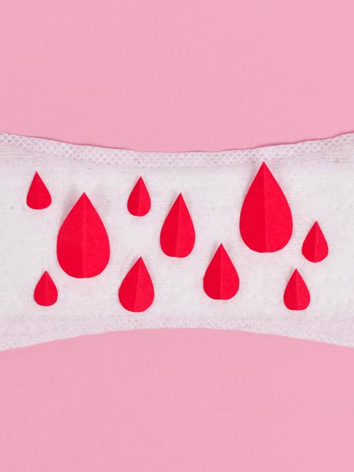 Aufnahme einer Slipeinlage auf rosa Untergrund. Auf der Einlage sind kleine rote Blutstropfen aus Papier verteilt.