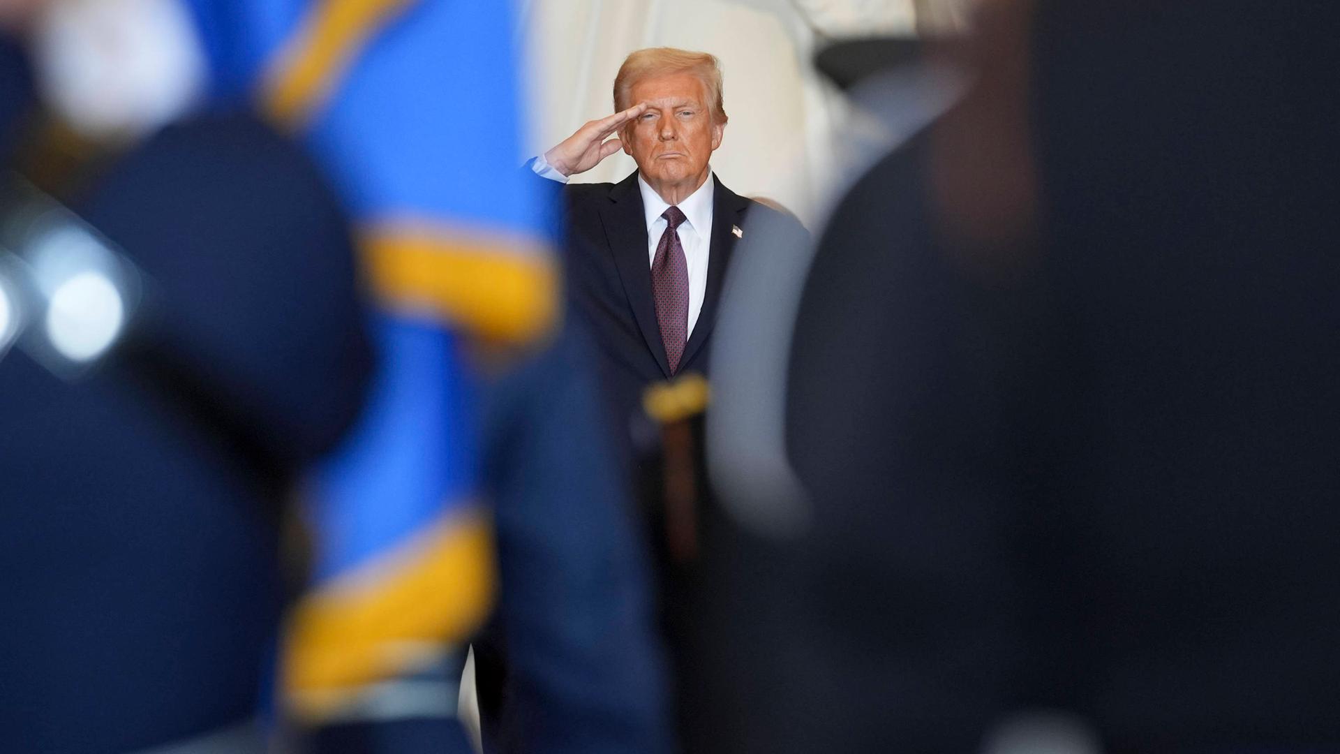 Links und rechts stehen Personen in Uniform. Zwischen ihnen ist eine Lücke. Der Blick fällt durch die Lücke auf US-Präsident Trump, der salutiert. Es ist die Amtseinführung von Trump am 20.01.2025.