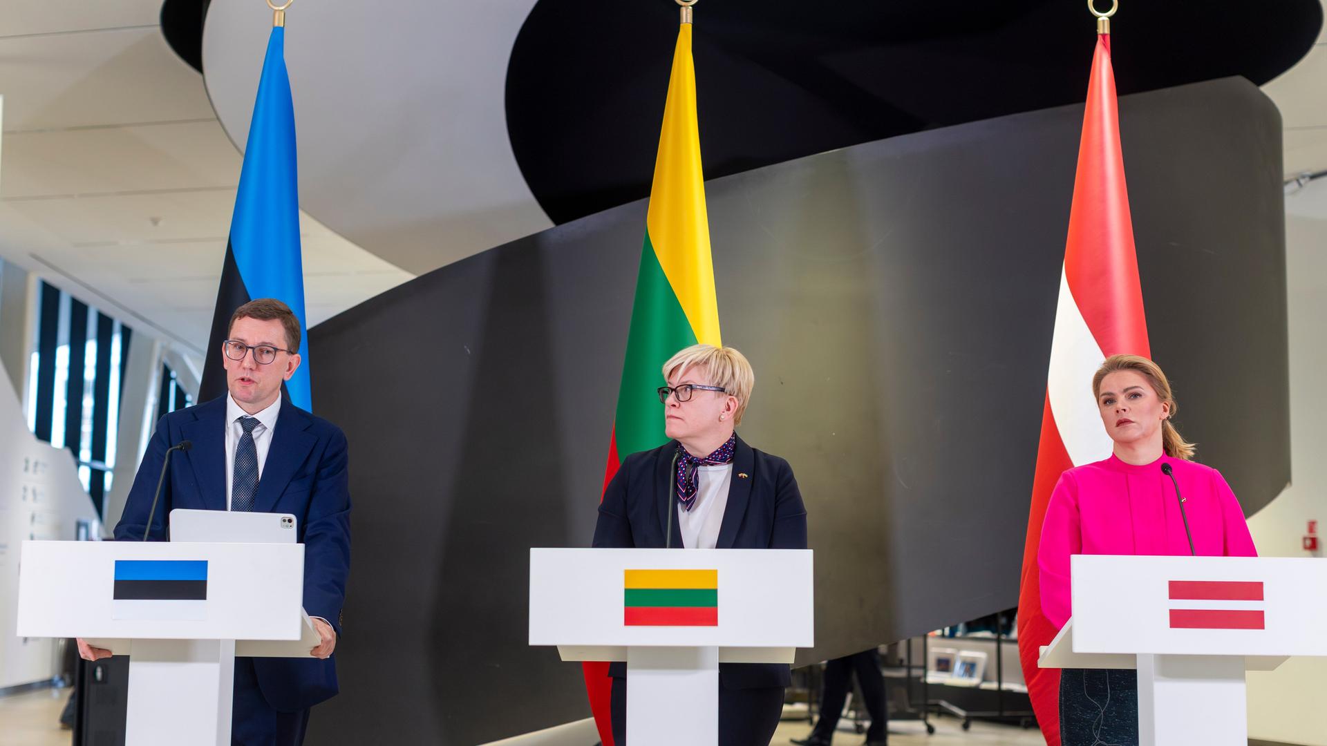 Die Premierminister der balatischen Staaten Estonia, Litauen und Lettlands, Michal, Simonyte und Silina stehen hinter Rednerpulten. Hinter ihnen die jeweiligen Landesfahnen.