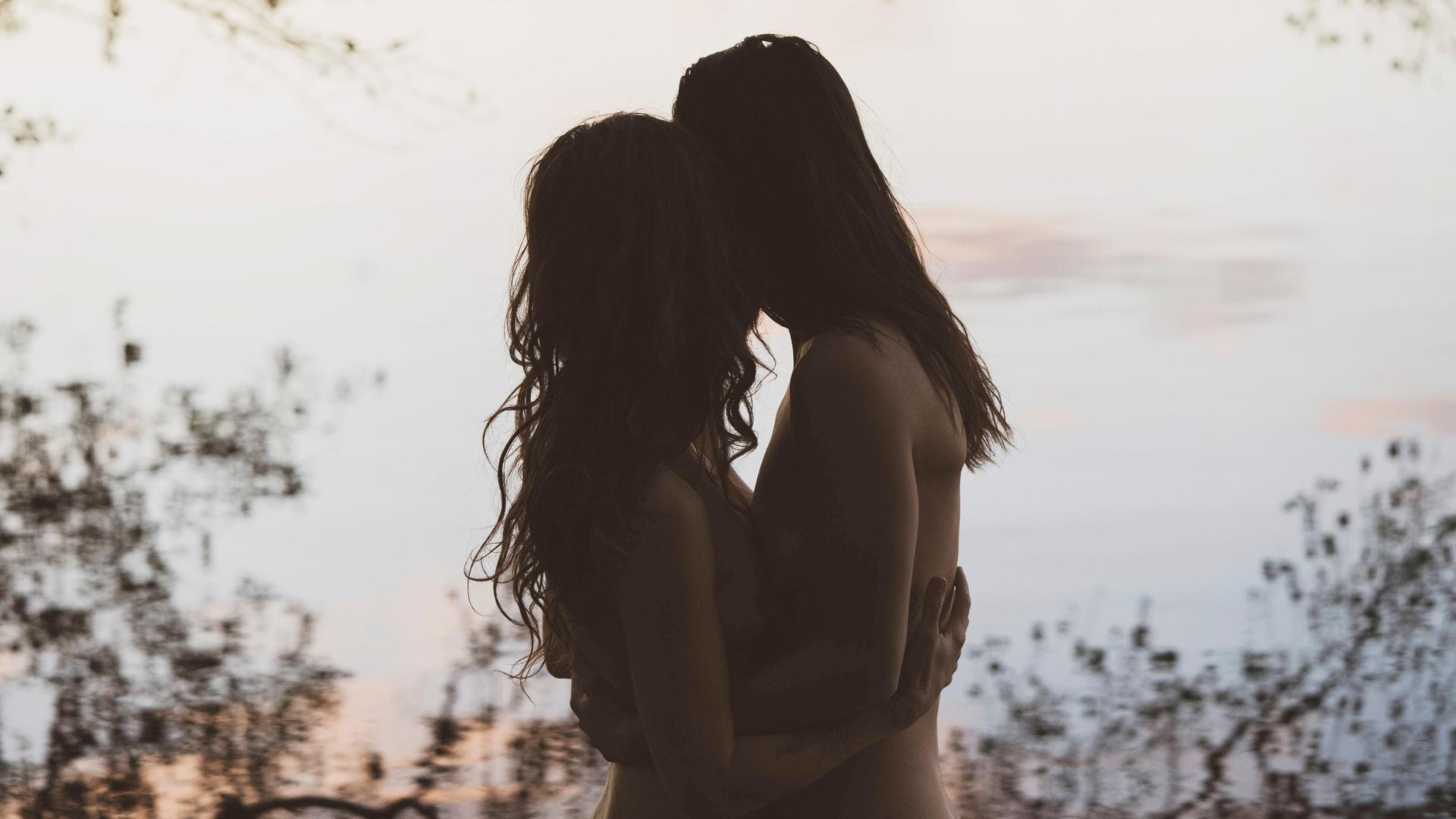 Die Silhouette eines Frauenpaares die sich umarmen, in romantischer Lichtstimmung vor einem See in Brandenburg.