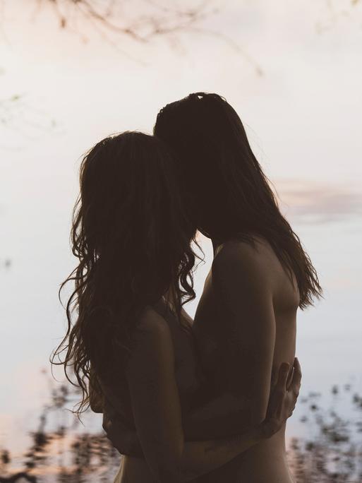 Die Silhouette eines Frauenpaares die sich umarmen, in romantischer Lichtstimmung vor einem See in Brandenburg.