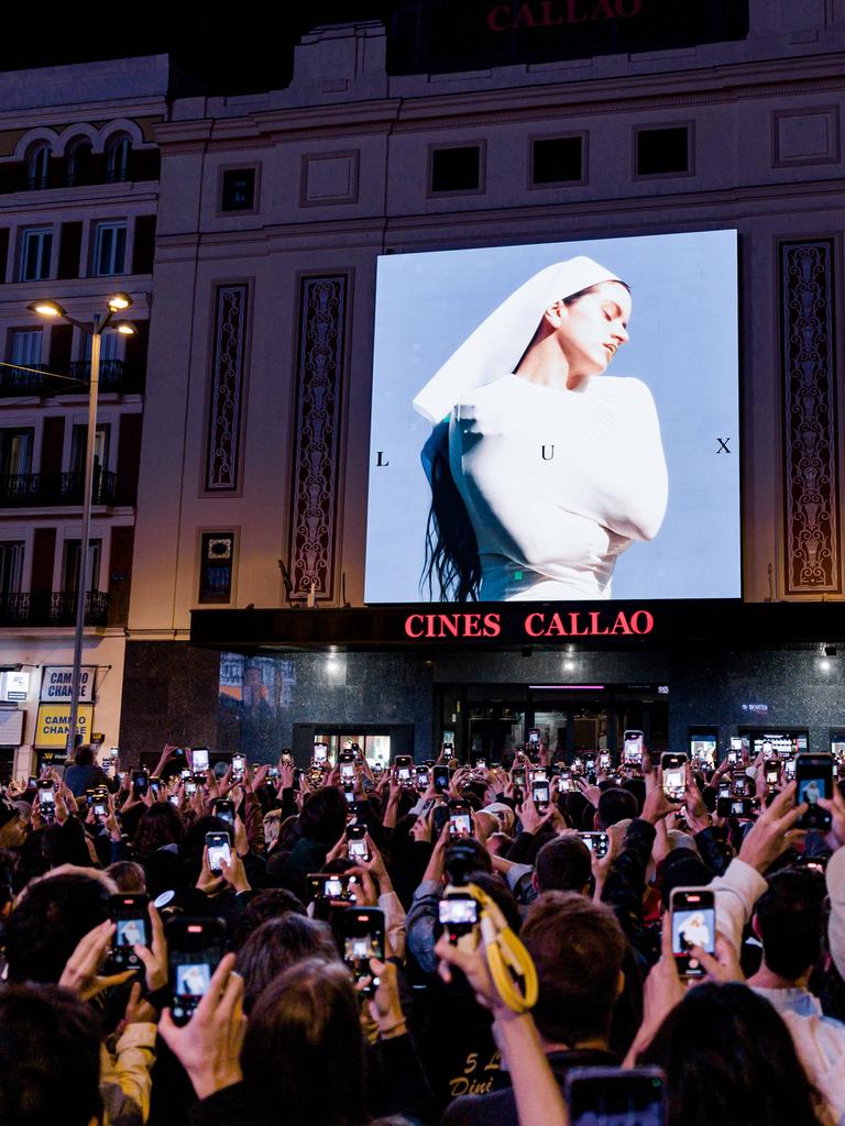 Eine auf einem Platz versammelte Menschenmenge fotografiert mit Smartphones das Cover von Rosalías aktuellem Album.