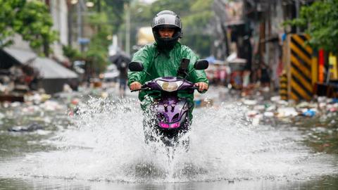 Ein Mann fährt mit einem Motorrad durch eine geflutete Straße.