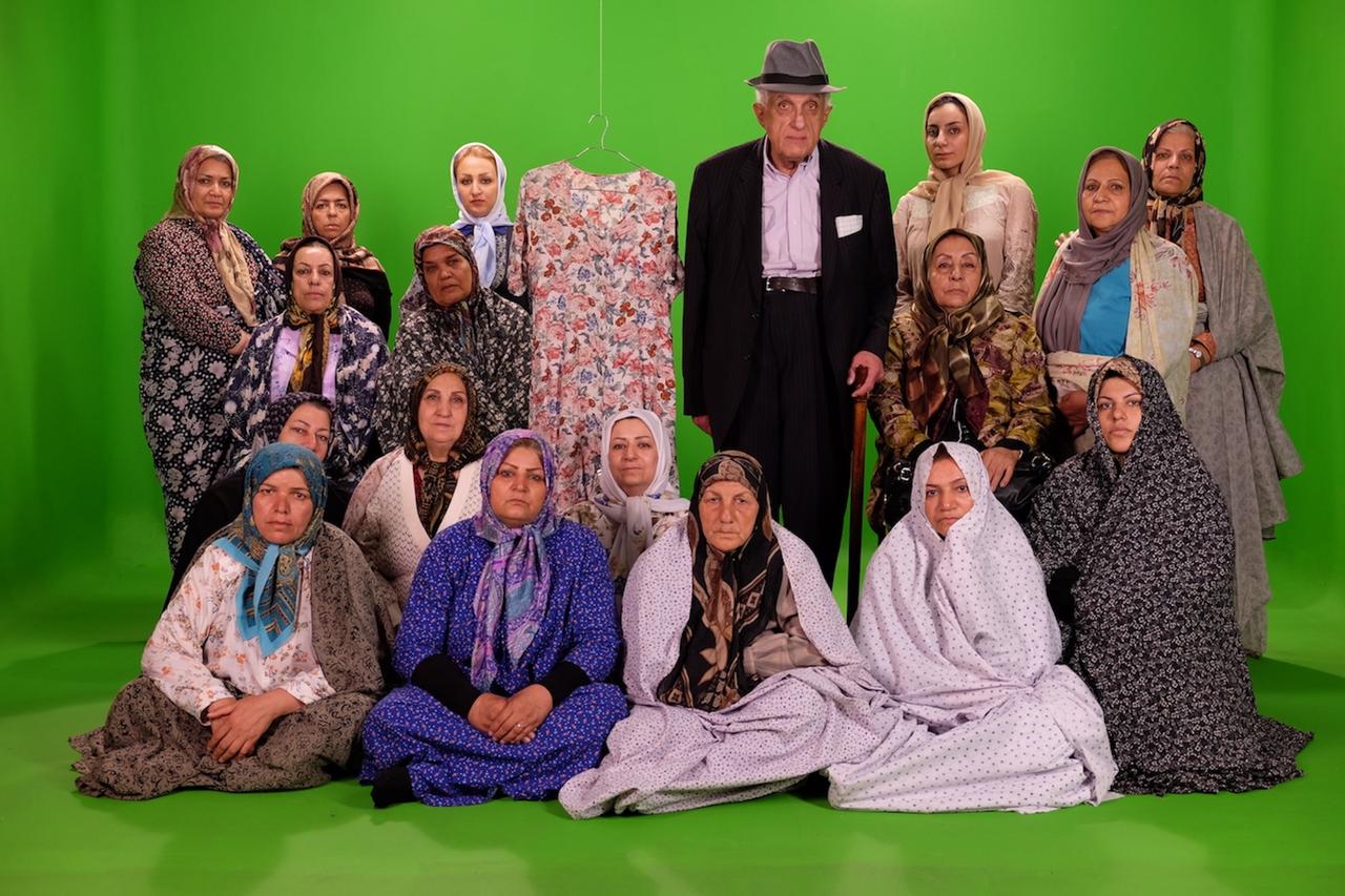 Szenenbild aus Farahnaz Sharifis Dokumentarfilm "Missing". Zu sehen sind vor grünem Hintergrund ältere Herrschaften, fast ausschließlich Frauen. Ein Mann mit Hut und leicht gebeugtem Rücken blickt leicht abwesend in die Kamera, die Frauen, allesamt mit Kopftuch, schauen ebenfalls recht resigniert. 