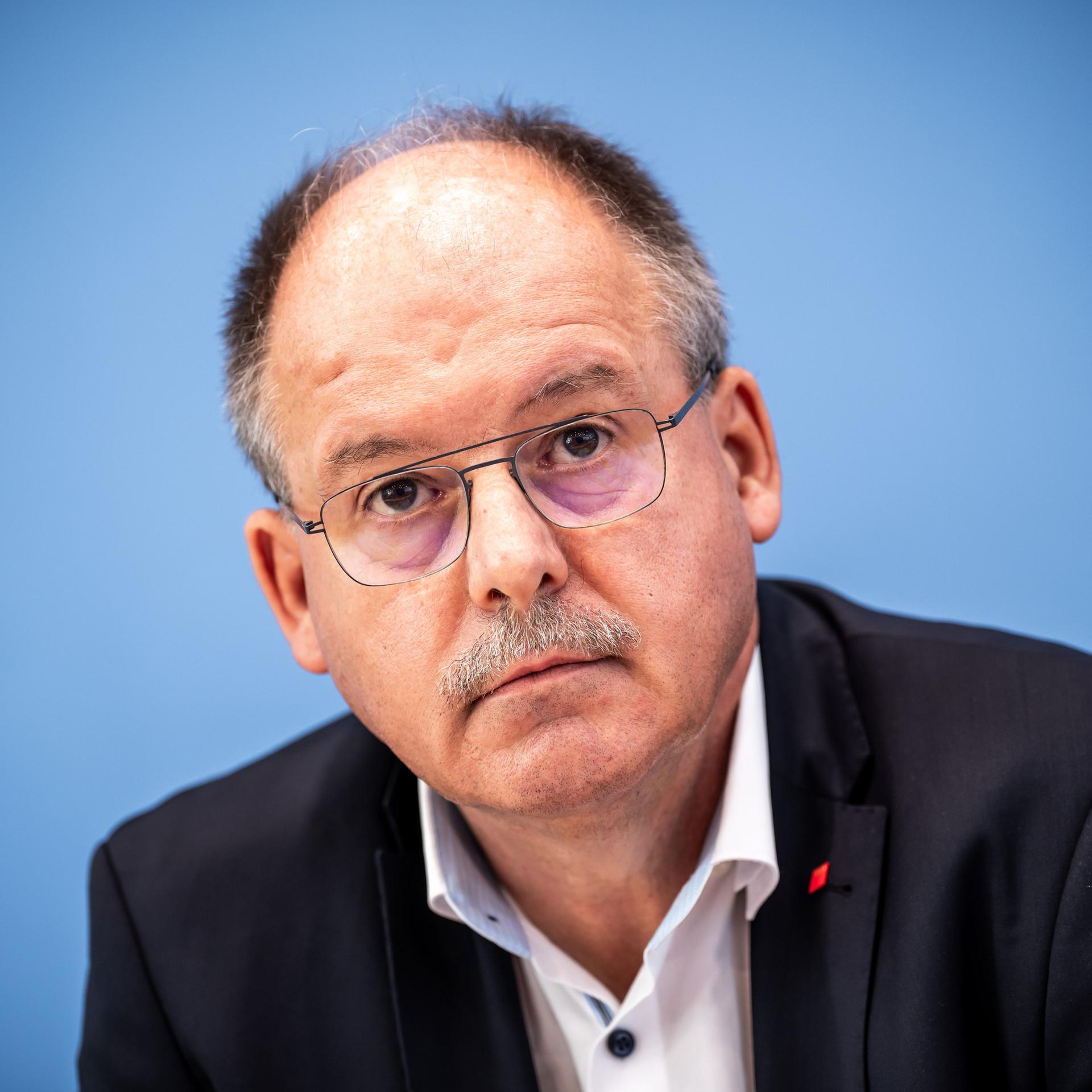 Stefan Körzell vom Deutschen Gewerkschaftsbund sitzt bei der Pressekonferenz nach der Entscheidung der Mindestlohnkommission vor einer blauen Wand