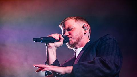 Kae Tempest bei einem Auftritt am 26.10.2025 in Bologna. Kae Tempest trägt einen Anzug, rappt in ein Mikro und gestikuliert mit der anderen Hand.