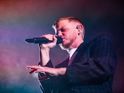 Kae Tempest bei einem Auftritt am 26.10.2025 in Bologna. Kae Tempest trägt einen Anzug, rappt in ein Mikro und gestikuliert mit der anderen Hand.