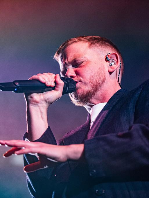 Kae Tempest bei einem Auftritt am 26.10.2025 in Bologna. Kae Tempest trägt einen Anzug, rappt in ein Mikro und gestikuliert mit der anderen Hand.