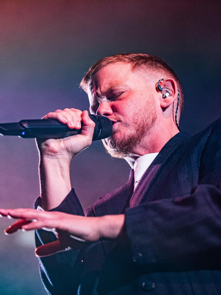 Kae Tempest bei einem Auftritt am 26.10.2025 in Bologna. Kae Tempest trägt einen Anzug, rappt in ein Mikro und gestikuliert mit der anderen Hand.