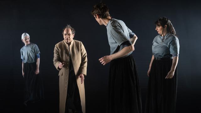 Vier Schauspieler auf einer spärlich beleuchteten Bühne.