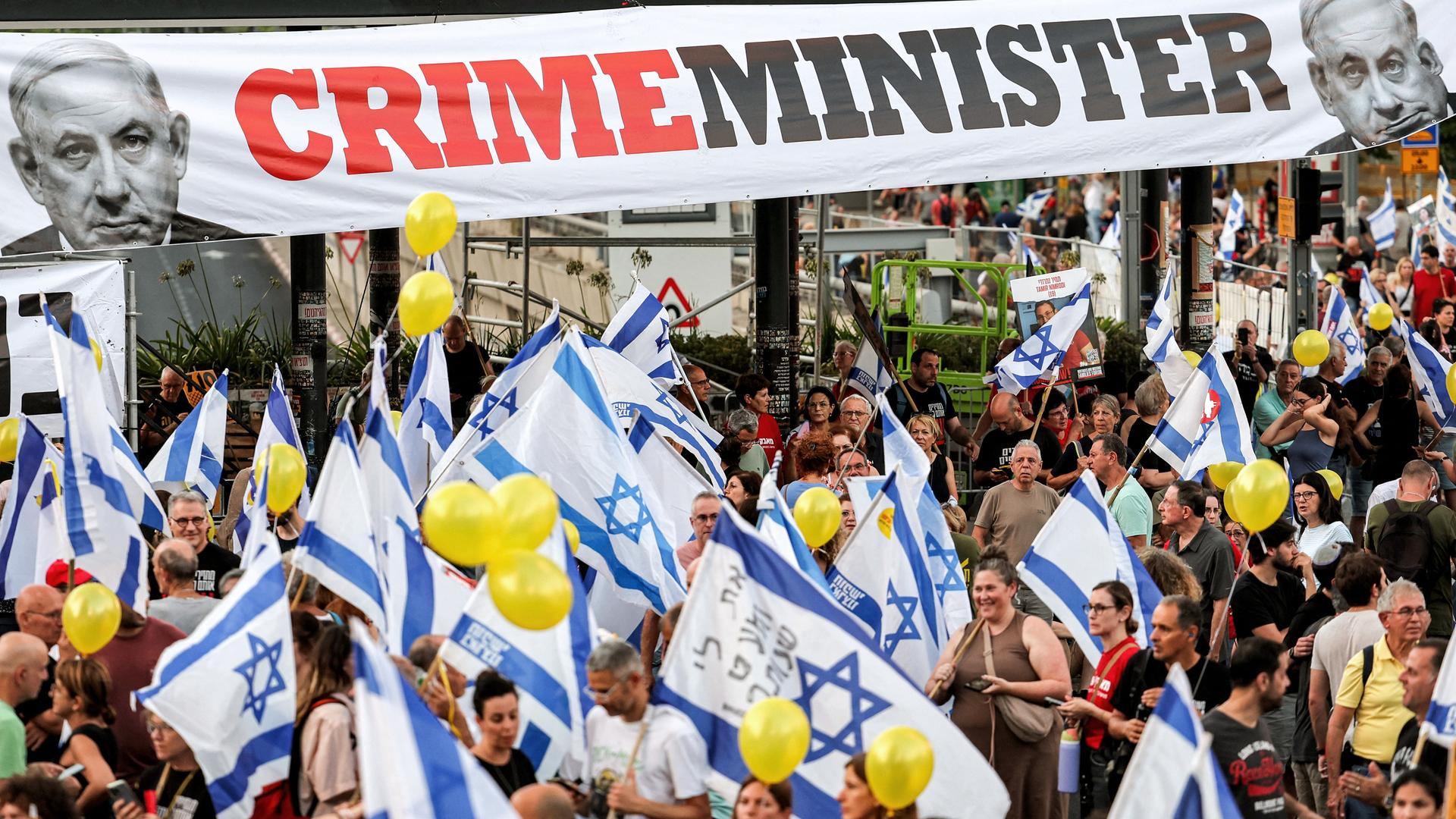 Über Demonstranten mit Israel-Fahnen hängt ein Banner mit einem Bild Netanjahus und der Aufschrift "Crime-Minister".